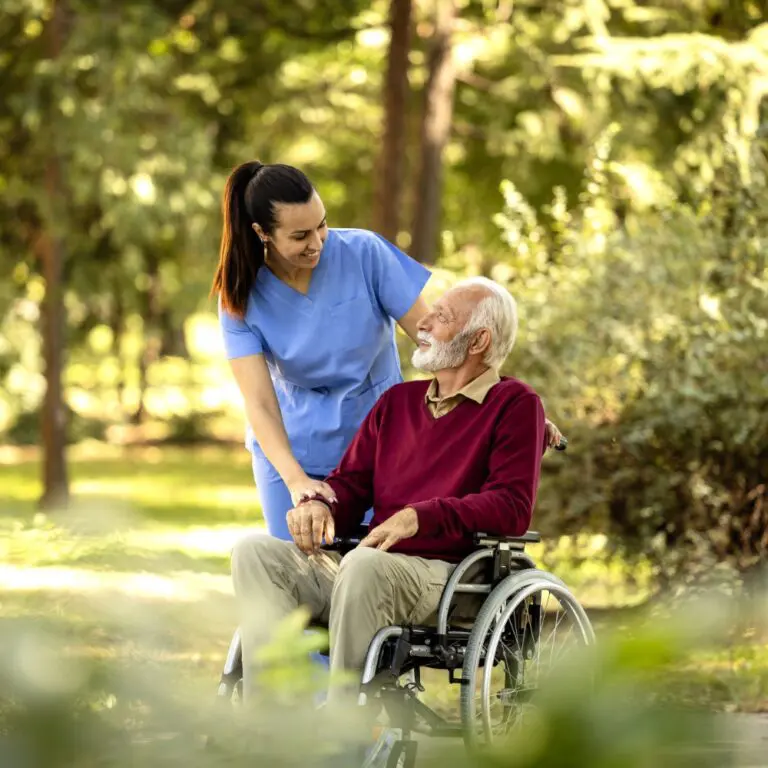 Nurse and elderly man in wheelchair going for a walk in the park.